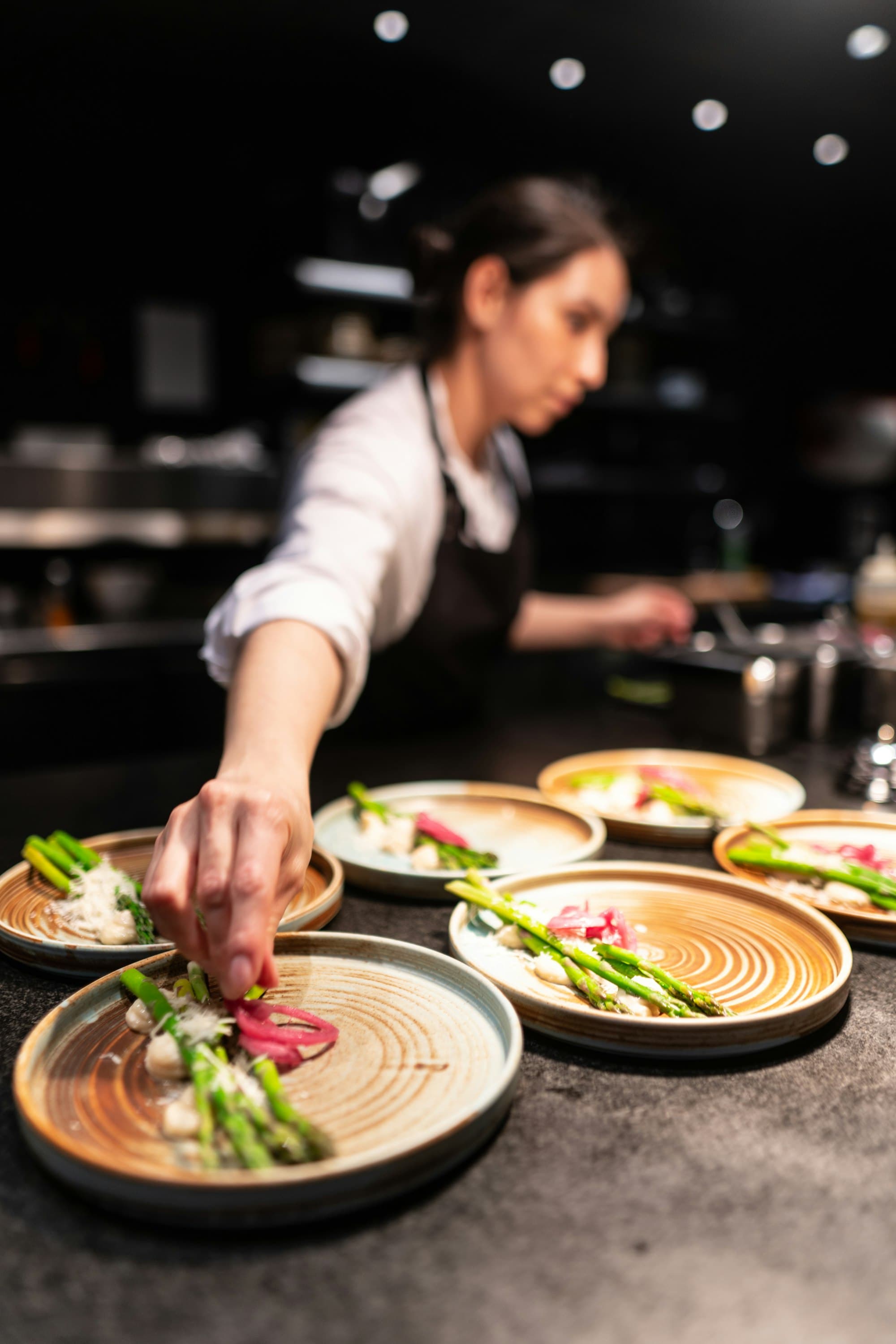 A cook finishes a row of asparagus dishes on the pass.