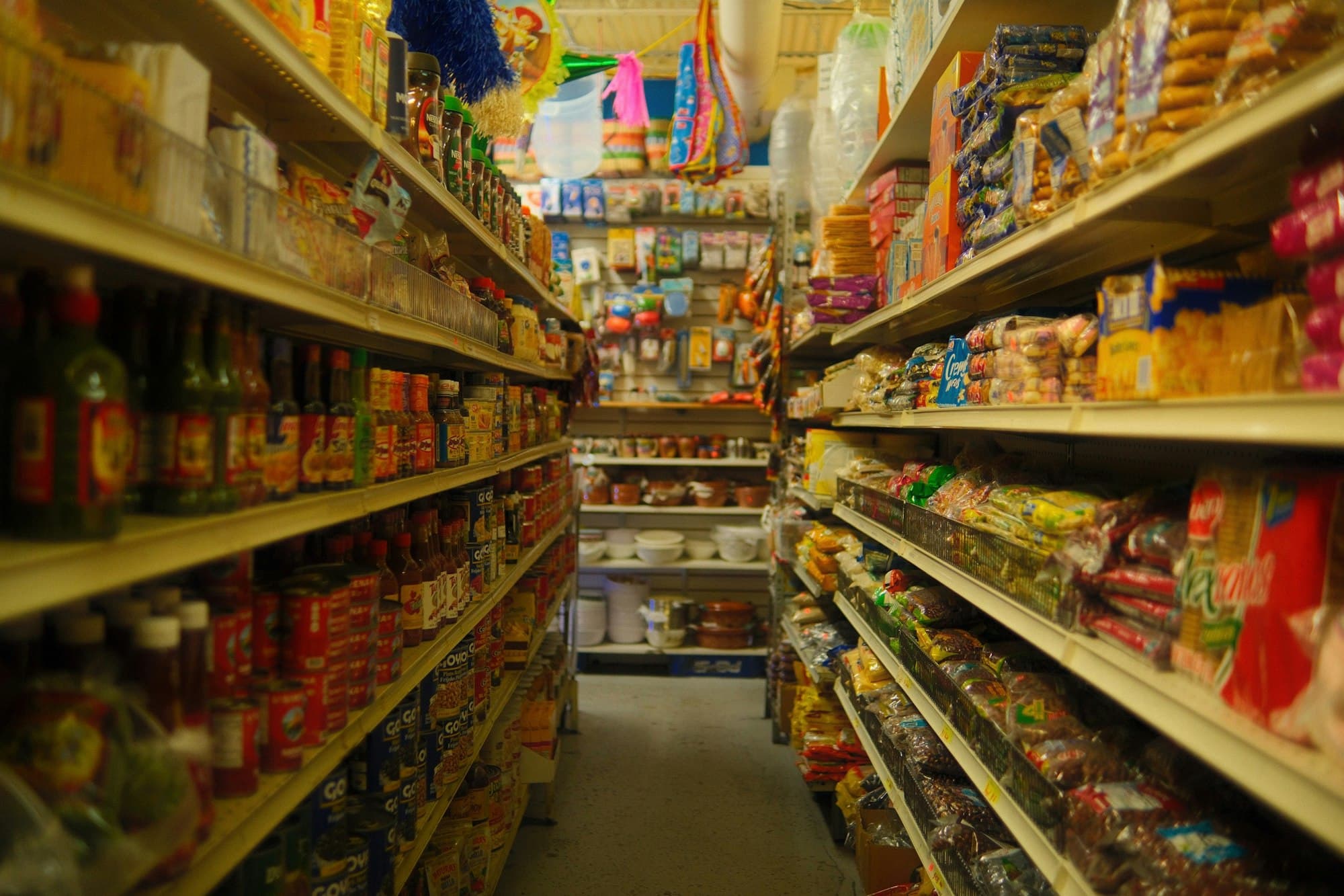 A narrow aisle in a local grocery shop, shelves stocked to the ceiling.