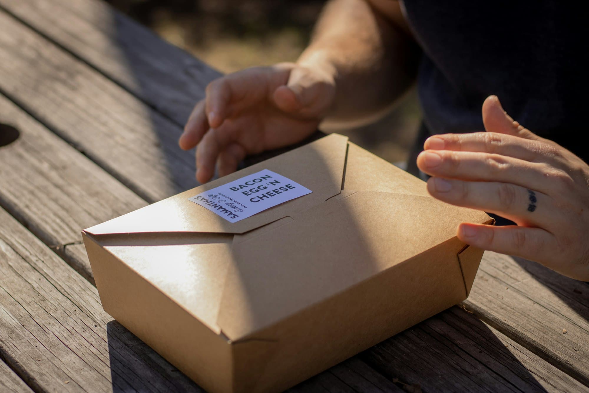 Hands closing a kraft takeaway box labelled with the order inside.