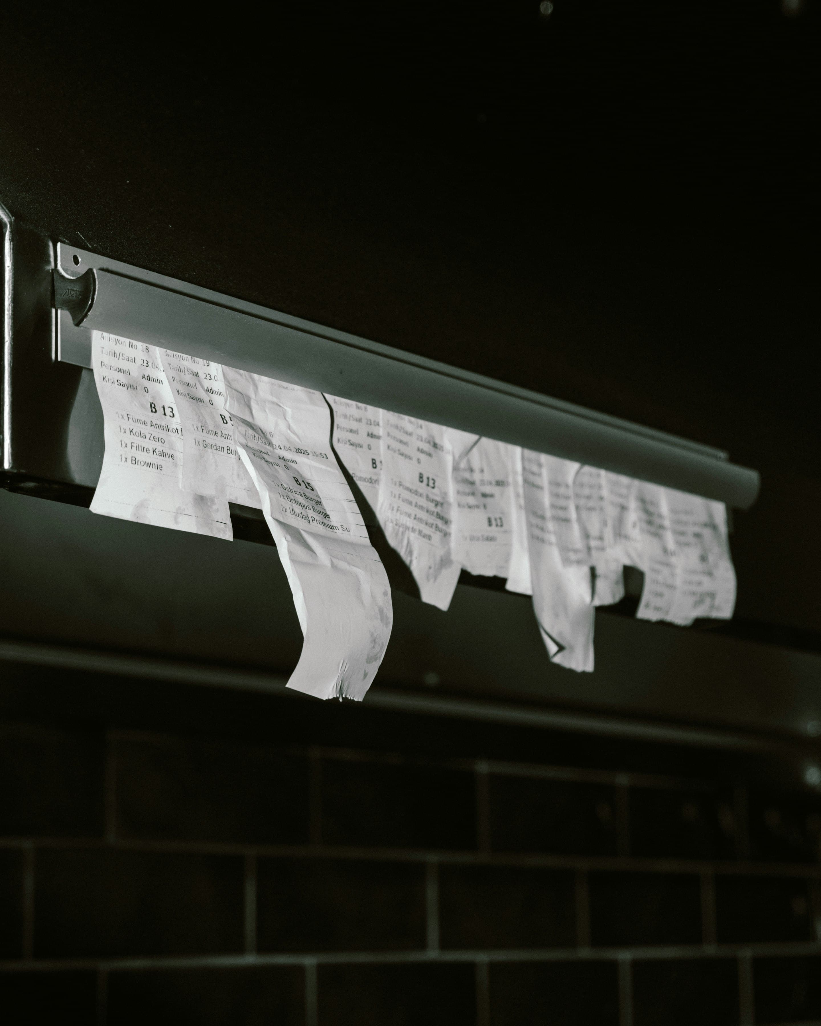 Torn order receipts hanging from a metal ticket rail in a dark kitchen.