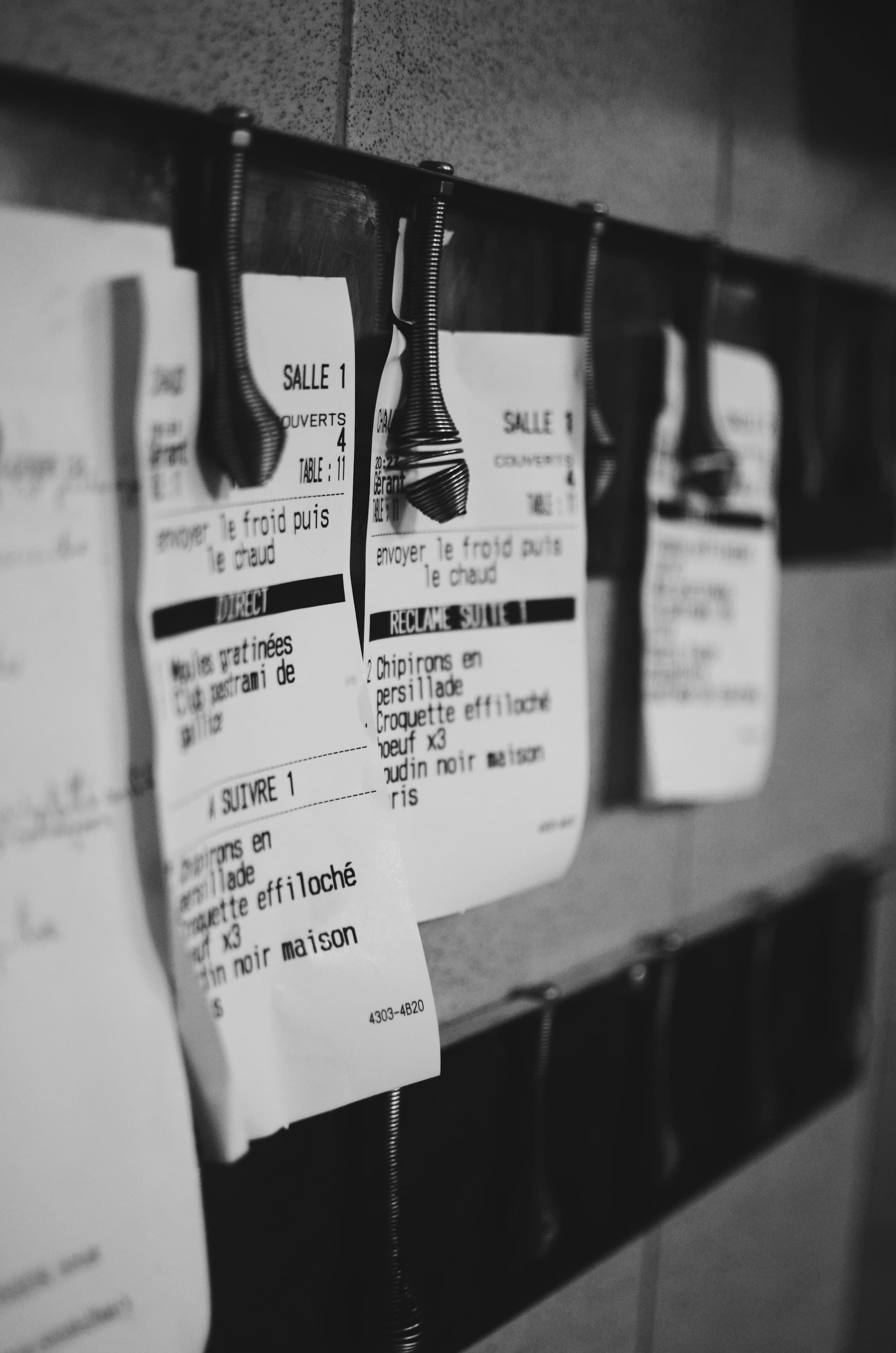 Printed kitchen tickets clipped to the rail, listing courses and table numbers.